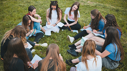 一群女学生坐在草地上的圆圈里 用笔记本进行集体工作潮人女性家庭作业教育青少年公园场地友谊技术朋友们图片