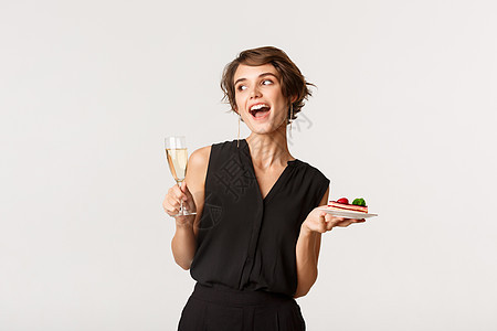 快乐迷人的女人参加庆祝派对 拿着一杯香槟和一块蛋糕 站在白色背景上图片