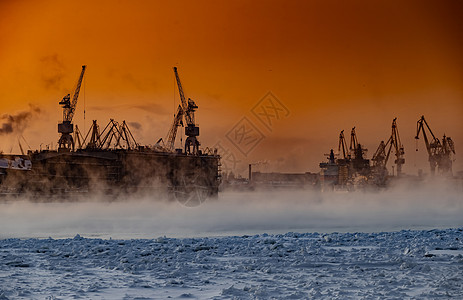 神奇日落时建造核破冰船 寒冷冬日波罗的海造船厂的起重机 涅瓦河上的蒸汽 光滑的河面 橙色的天空渔船货物技术船厂出口货轮码头送货城图片