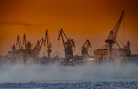 神奇日落时建造核破冰船 寒冷冬日波罗的海造船厂的起重机 涅瓦河上的蒸汽 光滑的河面 橙色的天空货轮码头送货港口商业海洋渔船船厂城图片