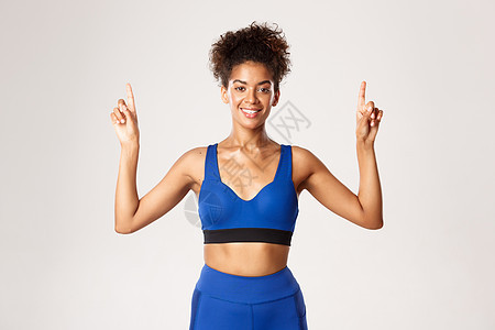 锻炼和健身的概念 微笑健康的非洲裔美国女运动员 穿着蓝色制服 手指向上 展示标志 白色背景图片