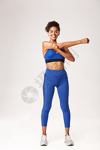 全长美丽微笑的非洲裔美国女运动员 穿着蓝色运动服 锻炼前热身 展示伸展运动 白色背景福利女孩深色活力训练有氧运动运动装衣服耐力力背景图片