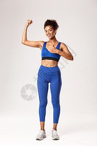 身穿蓝运动服 举起拇指和柔力比塞斯 建议体操锻炼 良好培训课 白背景的全身强壮有吸引力的美国女运动员图片