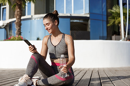 健身 饮用水和看智能手机后坐在地板上的快乐而有吸引力的女运动员在户外拍到的一张照片运动技术跑步赛跑者天空女性成人行动慢跑者有氧运图片