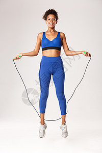穿着蓝运动服 满身微笑的女运动员 跳过绳索 看着快乐 在白种背景下锻炼出气来图片