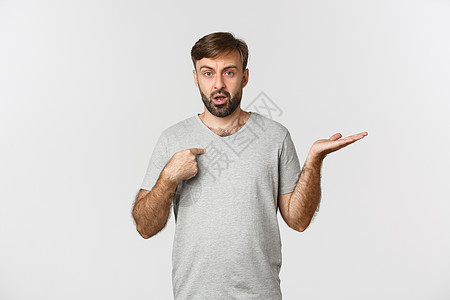 穿着灰色T恤的英俊长胡子男子的肖像 指着自己 摇摆不定 被控告 站在白背景之上商业成功发型情绪工作室衬衫胡须广告困惑学生图片