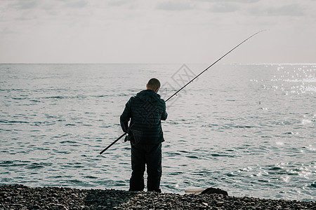 海上钓鱼的人爱好收紧鱼线卷轴 平静的海面 渔夫的特写镜头用手在鱼竿上扭动渔线轮 在户外的蓝色大海中钓鱼活动支撑行动男人溪流闲暇荒图片