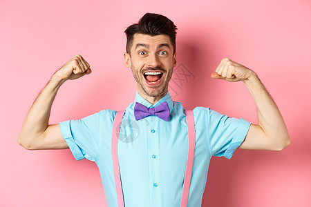 带着领领带和吊带微笑的caucasian男子 展示肌肉和感觉强健 有弹性的二头肌以炫耀 站在粉红色背景上吊带裤男人发型胡须商业情图片