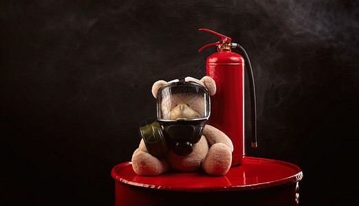 消防队的吉祥物是一只戴防毒面具的泰迪熊 背着黑暗背景烟雾中的灭火器气体火焰安全纪念品消防员玩具面具灭火消防队员阴霾背景图片