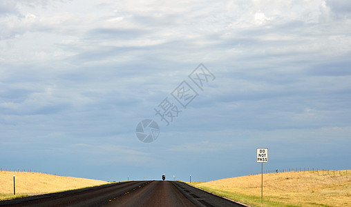 孤单骑自行车者在一条空旷的农村公路上 前方有“不准通行”标志图片