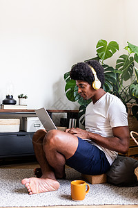 在客厅用笔记本电脑戴耳机的非洲青年男子 垂直图像 复制空间图片