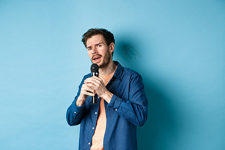 年轻男子用麦克风唱歌 玩卡拉OK 站在蓝背景上歌手成人成功胡子情绪男人生活胡须发型广告图片