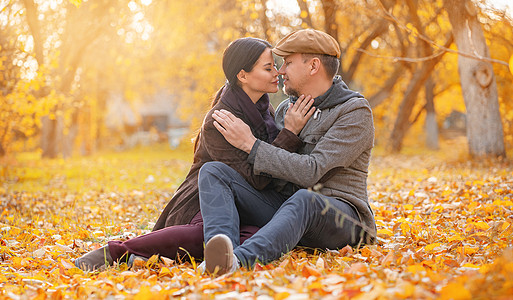 浪漫的情侣坐在秋天的落叶上 闭着眼睛 在秋天的郊区 好男人拥抱他心爱的女人 随意的风格 特写 秋天的背景图片
