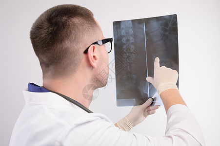 年轻的白人医生放射科医生正在看 X 光片 一位身穿白大衣 戴眼镜 带听诊器的医生手里拿着 X 光片医师工人专家白色药品从业者职业图片