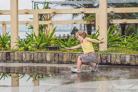 小男孩跑过水坑 夏天在户外公园跑步反射靴子童年外套孩子淋浴雨衣幸福图片