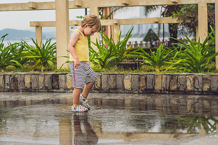 小男孩跑过水坑 夏天在户外好奇心孩子乐趣喜悦公园季节微笑飞溅童年靴子图片