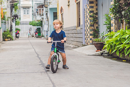 活跃的金发小孩男孩在城市的街道上驾驶自行车 蹒跚学步的孩子在温暖的夏日做梦和玩乐 儿童户外游戏 平衡车概念幼儿园安全练习头盔男生图片