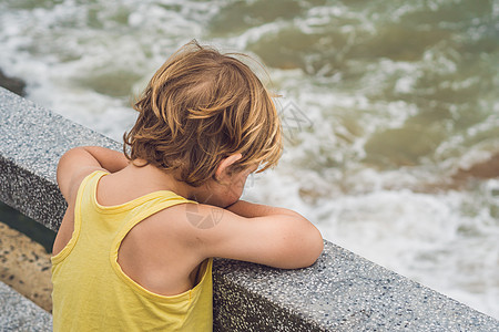 可爱的男孩站在岸边看海浪 看着海浪童年孤独岩石支撑游客旅行海洋青年假期海岸图片