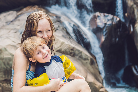 在瀑布背景上的母亲和小儿子 与孩子一起旅行的概念图片