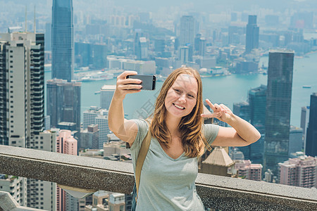 香港太平山女人用智能手机拍自拍杆照片 欣赏维多利亚港的景色 香港凌霄阁顶部的观景台 散焦背景 旅游亚洲概念自拍相机享受顶峰女士成图片