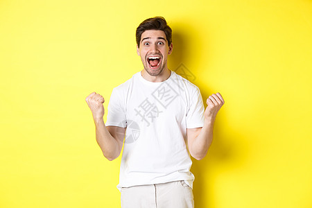 兴奋和幸运的男人赢了 握紧拳头 看着快乐 胜利和欢庆 站在黄色背景之上商业胡须手势优胜者成功成人广告学生男性情绪图片