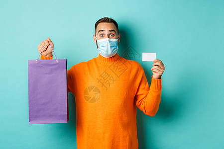 Covid19 大流行病和生活方式概念 快乐的男性客户展示信用卡和紫色购物袋 站在浅蓝背景上 光蓝背景促销情感胡子横幅潮人礼物广图片
