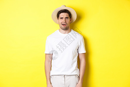旅游和夏季的概念 戴着草帽的迷茫男旅行者 站在黄色背景上 看起来很困惑 什么也听不懂男性手势潮人成人情绪旅行快乐假期胡须帽子图片