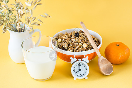 早餐健康 碗 牛奶杯 橙子 木勺和黄色背景的闹钟中烤面包面条图片