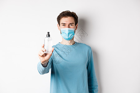 Covid19 健康和检疫概念 身戴医疗面具的年轻人伸出手来展示防疫剂 建议抗消毒 站在白色背景上站立广告消毒剂情绪工作室隔离社图片