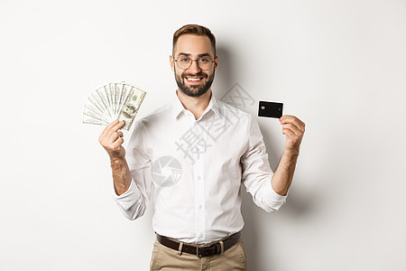 英俊的商务人士显示信用卡和货币美元 微笑满足 站在白背景上站立于一身横幅男人经理雇主经纪人头发广告成功标识工作图片