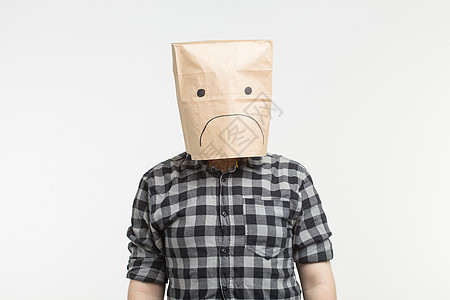 在白背景上头戴纸袋前 带着悲伤的表情的不快男子图片