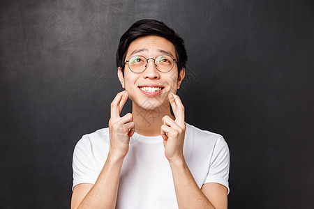 乐观 充满希望的亚洲年轻男子的特写 祝你好运 满怀希望和信念仰望天空 微笑着向上帝祈祷 恳求梦想成真 站在黑色背景中图片