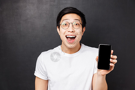 技术 消息传递和人的概念 特写 快乐 惊讶和印象深刻的年轻兴奋的亚洲男子身穿白色 T 恤 展示智能手机显示屏上惊艳的酷应用图片