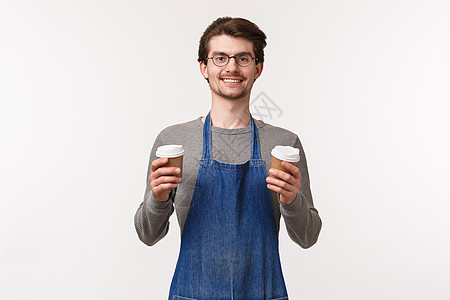 帅气友善 面带微笑的年轻白人男性员工 穿着围裙的咖啡店老板点了外卖 拿着两杯饮料 给顾客他们的饮料 白色背景图片