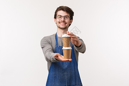 友好开朗的年轻男员工穿着围裙的肖像 在咖啡店工作 给顾客点了两杯饮料 准备了卡布奇诺咖啡 微笑着说享受你的饮料图片