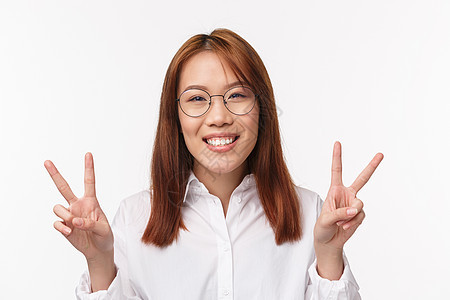 戴眼镜的快乐亚洲女性的特写 微笑的卡瓦伊表现出和平姿态 善意的标志 表达积极的幸福和快乐 站在光明的一面 站在白色背景图片