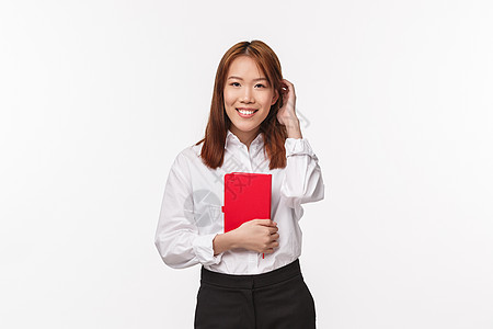 商业 金融和职业概念 身穿白衬衫和黑裙的年轻可爱亚洲女办公室女士的画像 手持红色笔记本规划器 微笑着害羞地摸着头发脸红图片