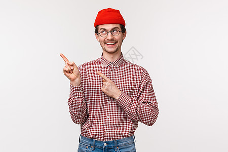 戴着眼镜和红色帽子的快乐微笑的极客男人的腰部肖像 指着左上角 脸上带着高兴的笑容 满意地找到了好产品 推荐使用这项服务图片