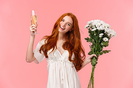 可爱 快乐 漂亮的红头发女人庆祝 参加令人敬畏的 b 日派对以纪念她 手捧白色花束 举杯香槟 欢呼 粉红色背景图片