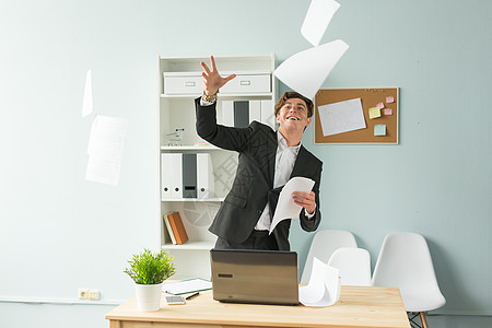商业 幽默和人的概念     英俊和年轻穿西装的男子在办公室里扔纸笔记本电脑马桶椅子总理府套装桌子架子微笑植物图片