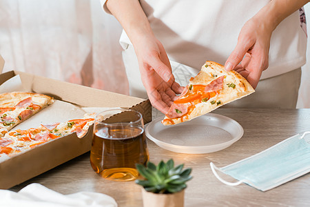 取出食物 一位女士将一片披萨放在一次性塑料盘中 并将一盒披萨放在厨房的桌子上图片