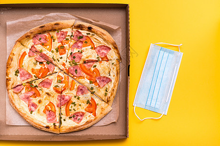 送外卖和交货 在纸板盒和黄色背景保护面罩中的即食披萨图片