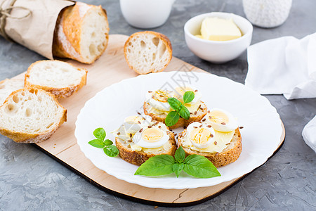 早上丰盛的早餐 桌上的盘子上放着新鲜的面包三明治 上面放着黄油 鹌鹑蛋 亚麻籽和罗勒籽图片