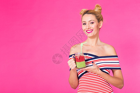 穿着明亮服装 拿着和喝着美味的绿色滑冰奶昔 以粉红背景与复制空间为背景的有趣的年轻女子肖像饮食玻璃女孩咖啡店乐趣工作室女性水果果图片