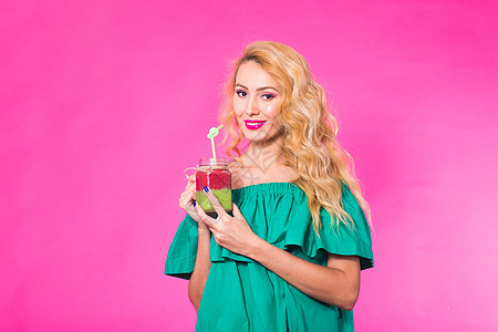 年轻女性在粉红背景上 抱着和喝着美味的绿色冰凉果奶昔的肖像青少年饮食水果潮人青年营养食物果汁乐趣工作室图片