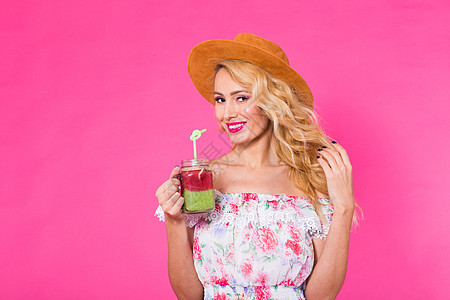 年轻女性在粉红背景上 抱着和喝着美味的绿色冰凉果奶昔的肖像饮料食物工作室稻草玻璃化妆品乐趣营养排毒青年图片