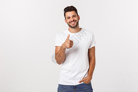 年轻快乐的男子与拇指举起标志 在空闲中孤立白背景衣服展示牛仔裤成人工作室优胜者衬衫男人手势幸福图片