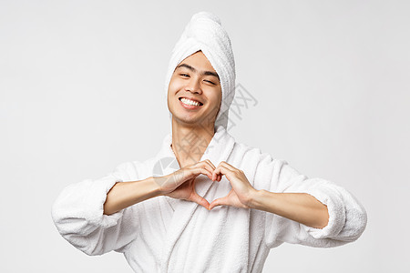 美容 水疗和休闲概念 穿着浴袍和浴巾的可爱的亚洲男人 在胸前展示心形标志 微笑着乐观 看起来很高兴 站在白色背景下快乐毛巾男性相图片
