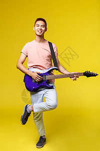 生活方式 休闲和青年概念 身穿粉色 T 恤 弹着电吉他 笑得开心 站在黄色背景中的热情帅气的亚洲少年垂直肖像乐队技术吉他手势互联图片