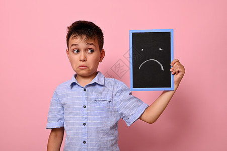 粉红色背景的孤立肖像 其中一位悲伤的中小学生在脸近处拿着一张带有感伤情绪的滑板图片